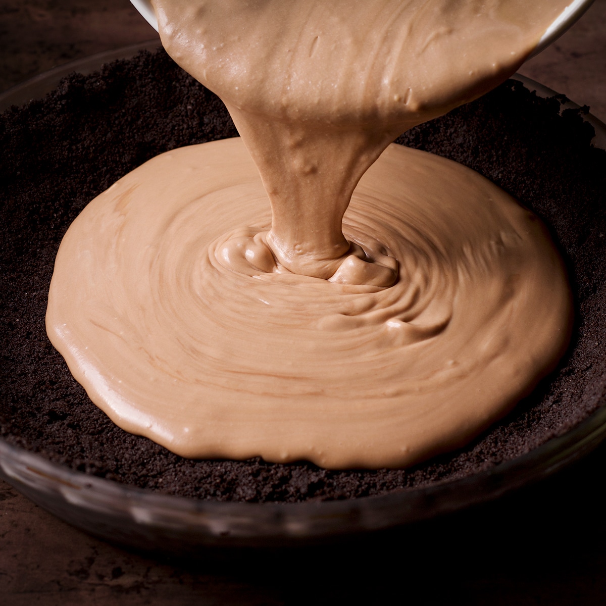 Someone pouring milk chocolate mousse into an Oreo cookie crust.