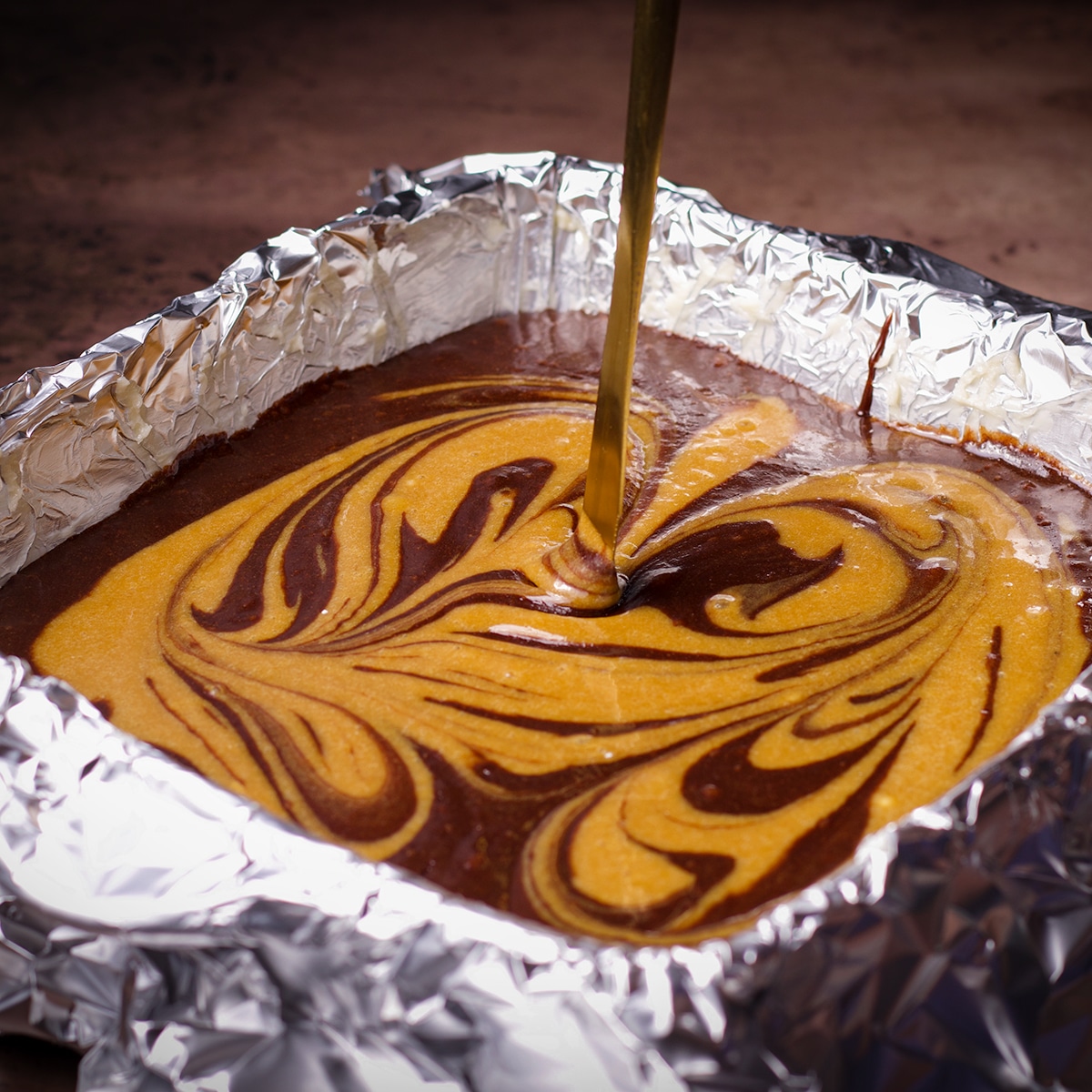 Someone using a knife to swirl tahini brownie batter into chocolate tahini brownie batter.