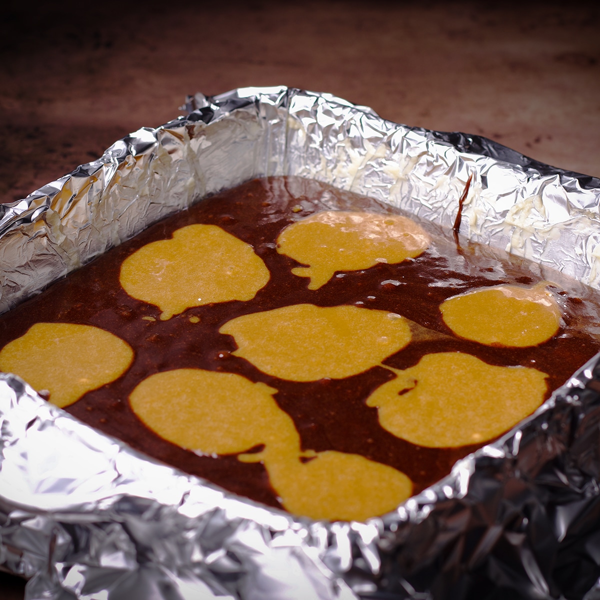 A pan filled with chocolate tahini brownie batter topped with dollops of tahini brownie batter.