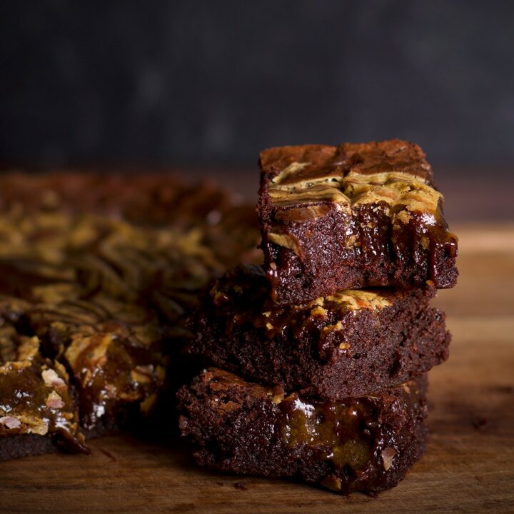Three tahini brownies stacked on a cutting board. The top brownie has a bite taken out of it.