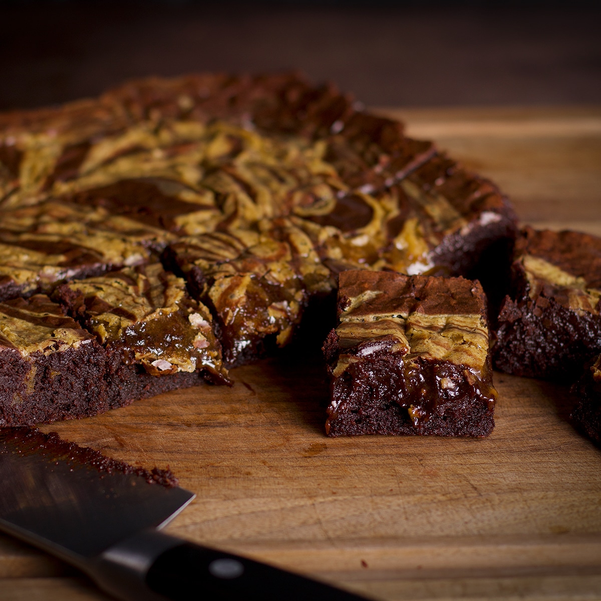 A cake of tahini brownies on a cutting board with a knife.