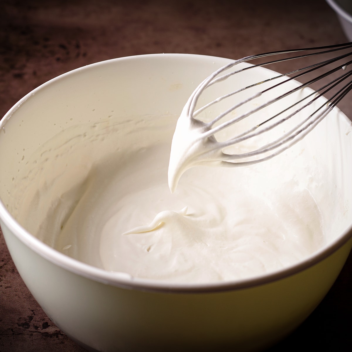 Someone lifting a whisk from a bowl of whipped cream to show that it's at the soft peak stage.