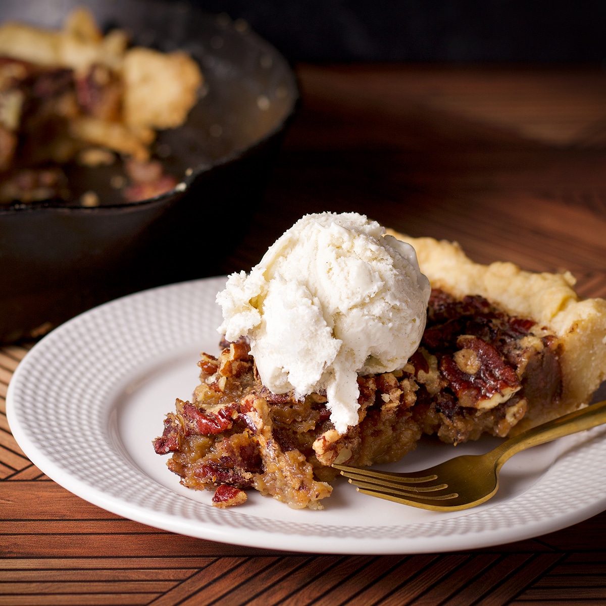A slice of pecan pie on a plate topped with a scoop of vanilla ice cream.