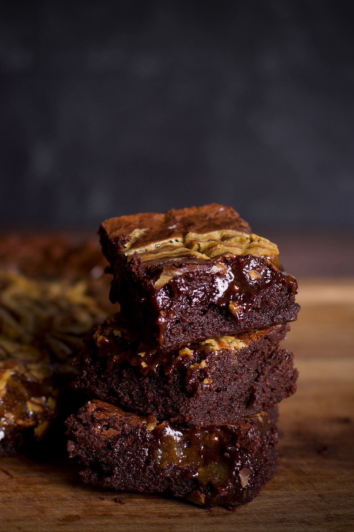 Three tahini brownies stacked on top of each other on a cutting board.