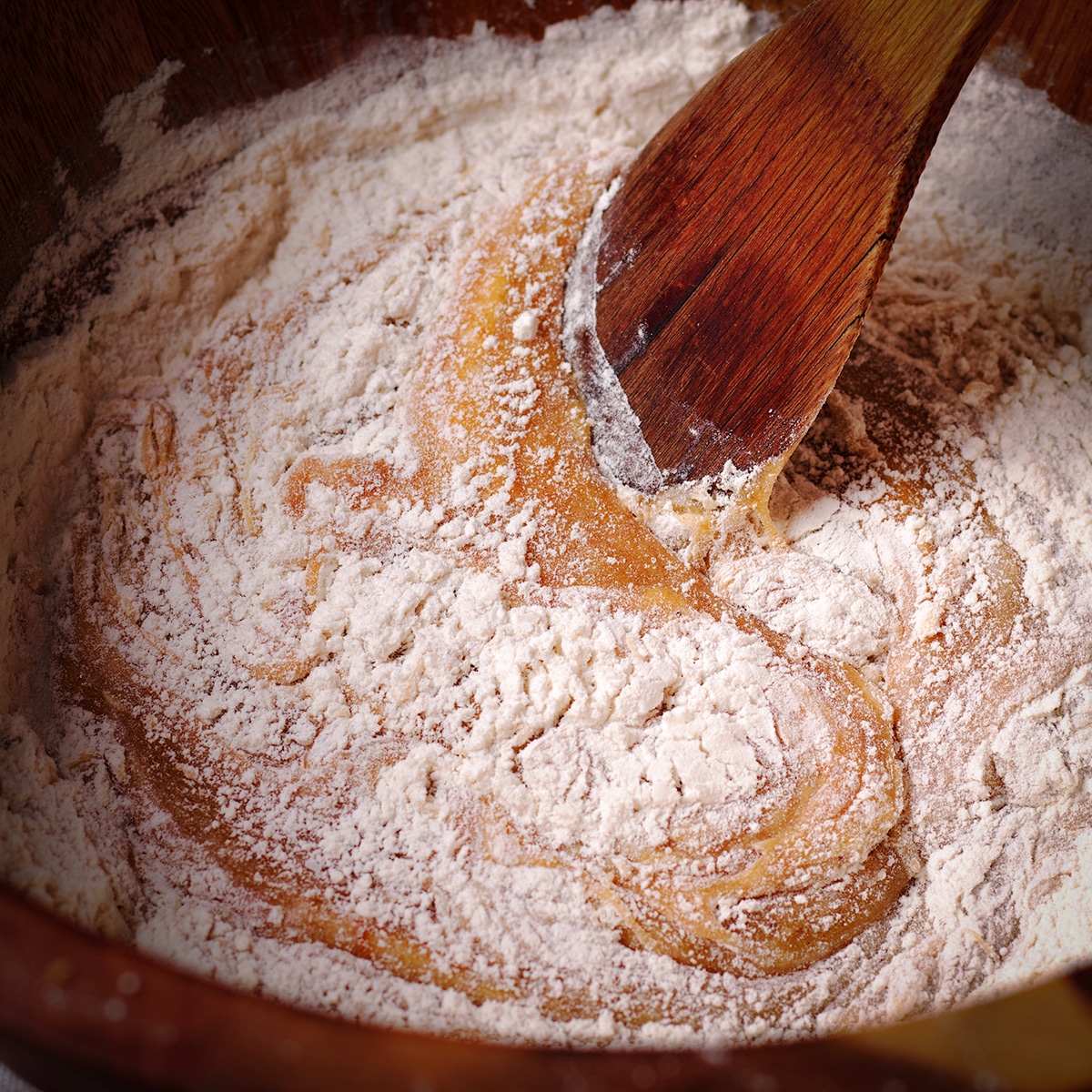 Using a wooden spoon to stir flour into the cake batter.