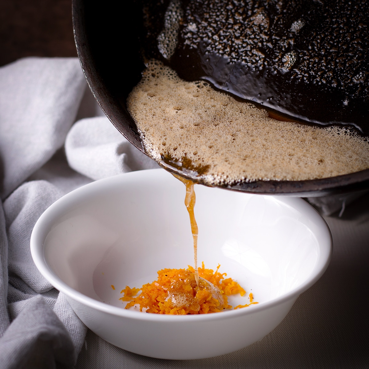 Pouring brown butter from a skillet into a white bowl containing orange zest and ground cloves.
