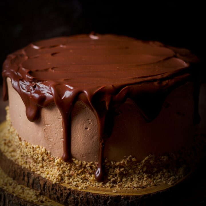 Chocolate ganache dripping over the sides of a chocolate truffle cake frosted with milk chocolate buttercream.