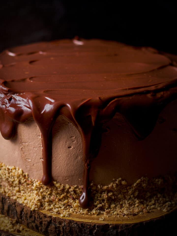 Chocolate ganache dripping over the sides of a chocolate truffle cake frosted with milk chocolate buttercream.