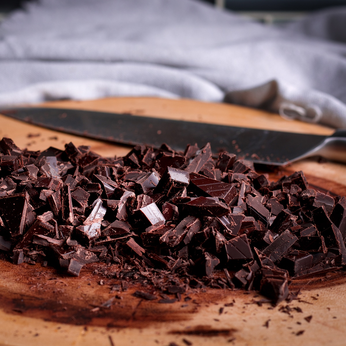 A pile of chopped chocolate on a cutting board with a knife resting next to it.