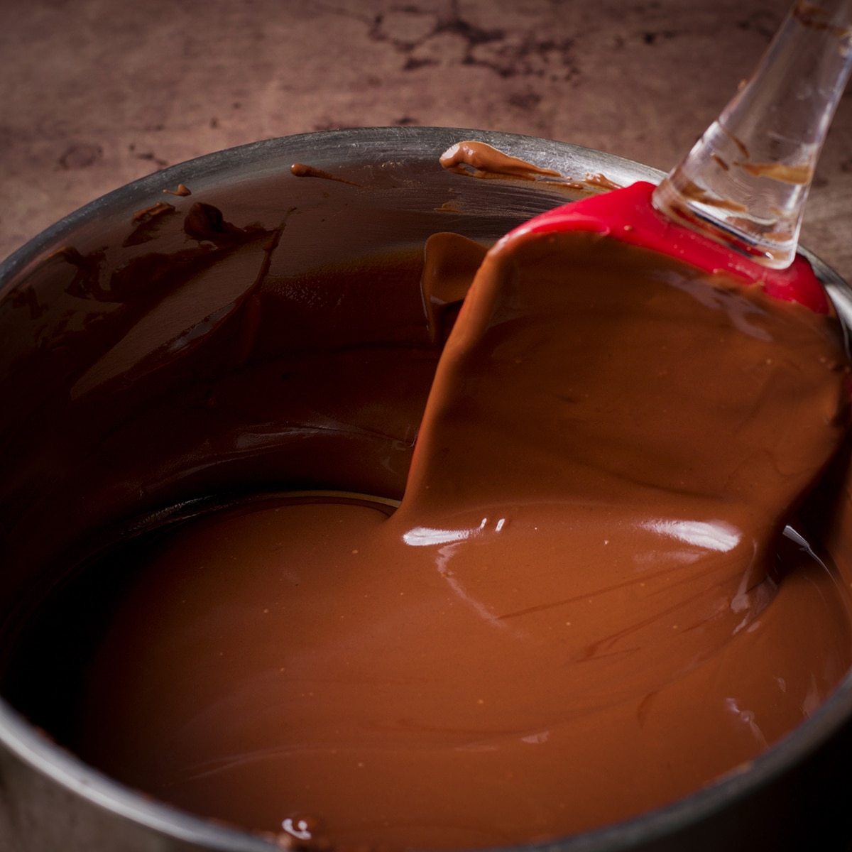Someone using a rubber spatula to stir melted milk chocolate in a saucepan.