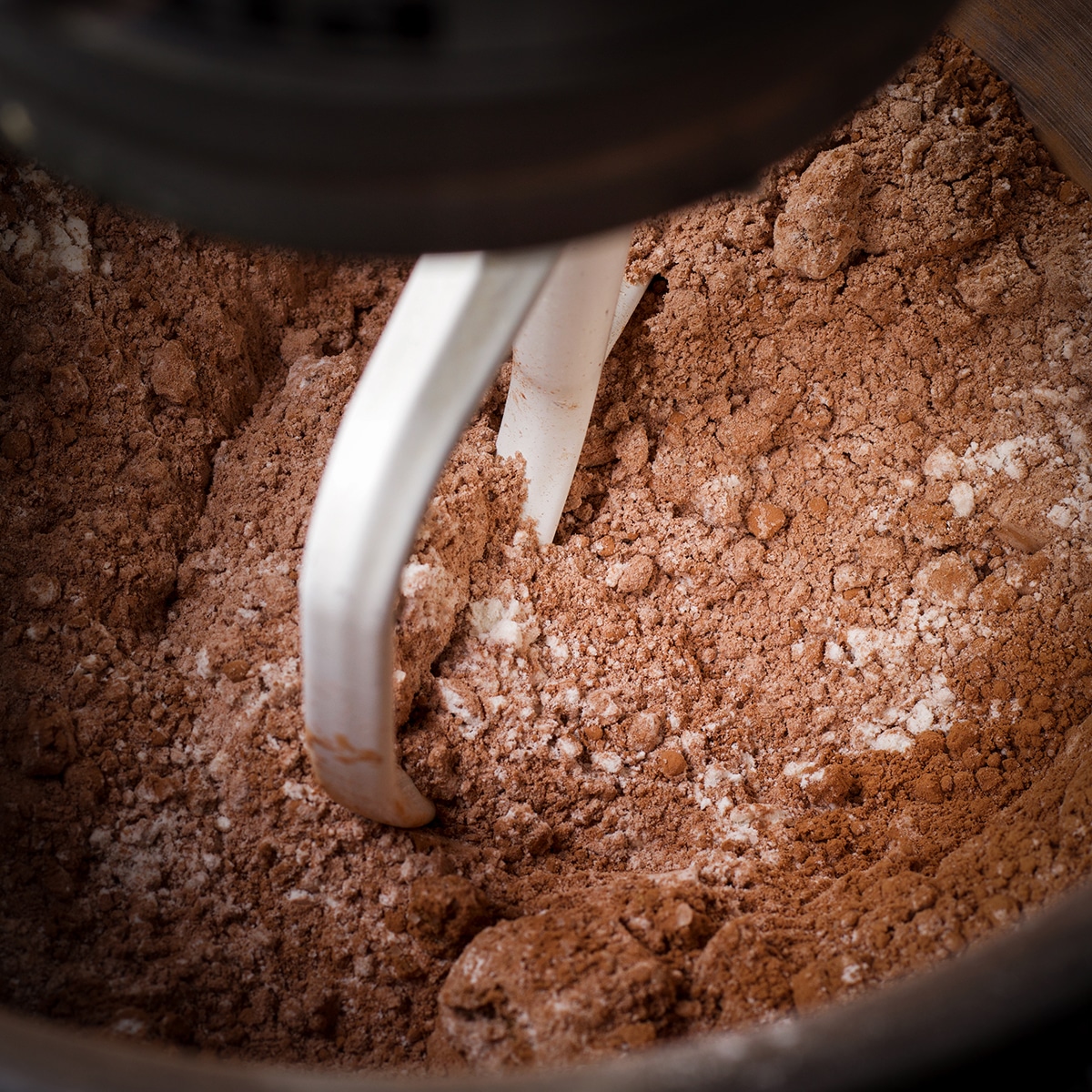 Using the paddle attachment on an electric mixer to blend sugar, flour, cocoa powder, salt, baking powder, and baking soda in a large bowl.