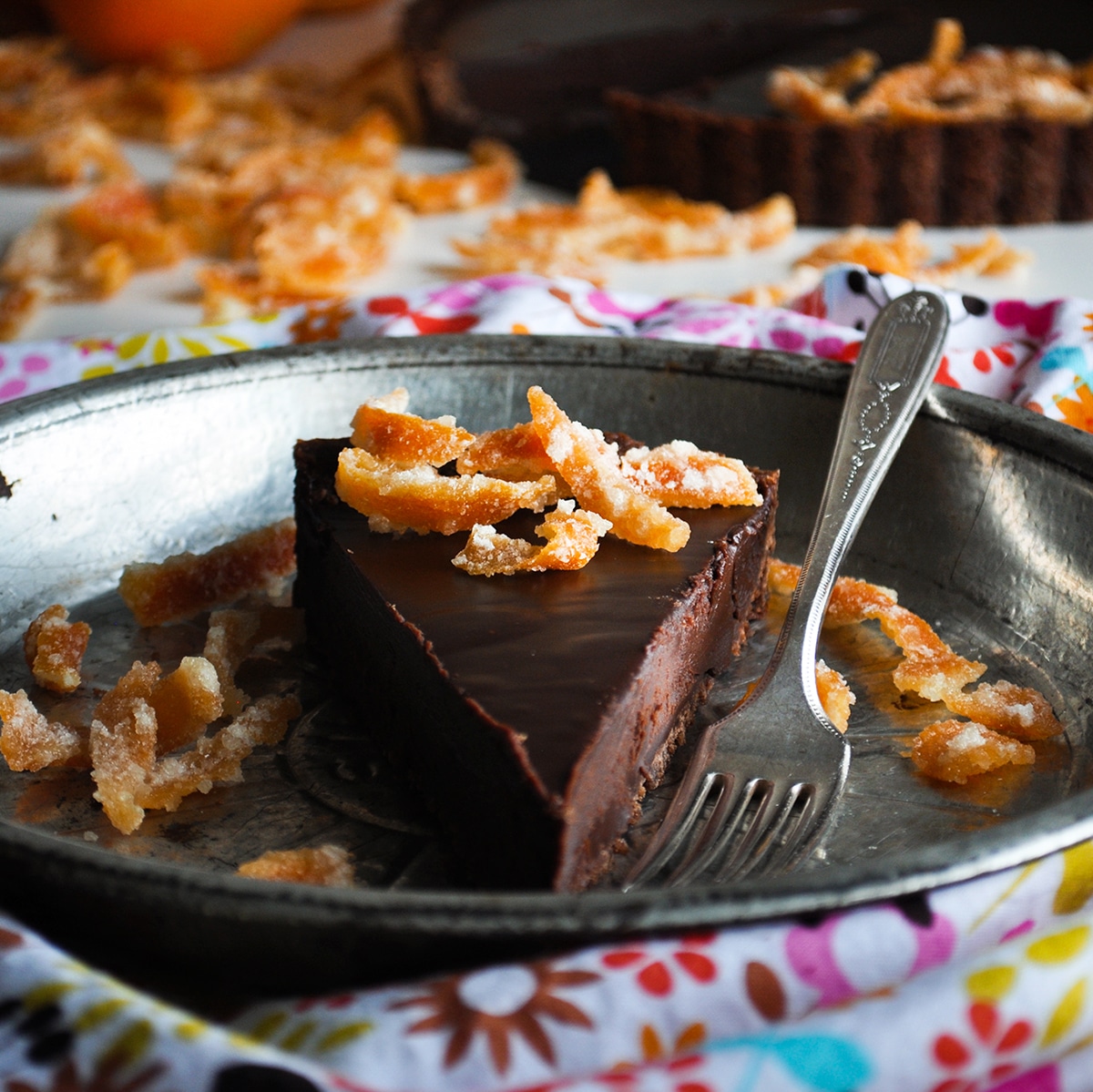 A slice of chocolate orange truffle tart decorated with candied orange peel on a tin plate.