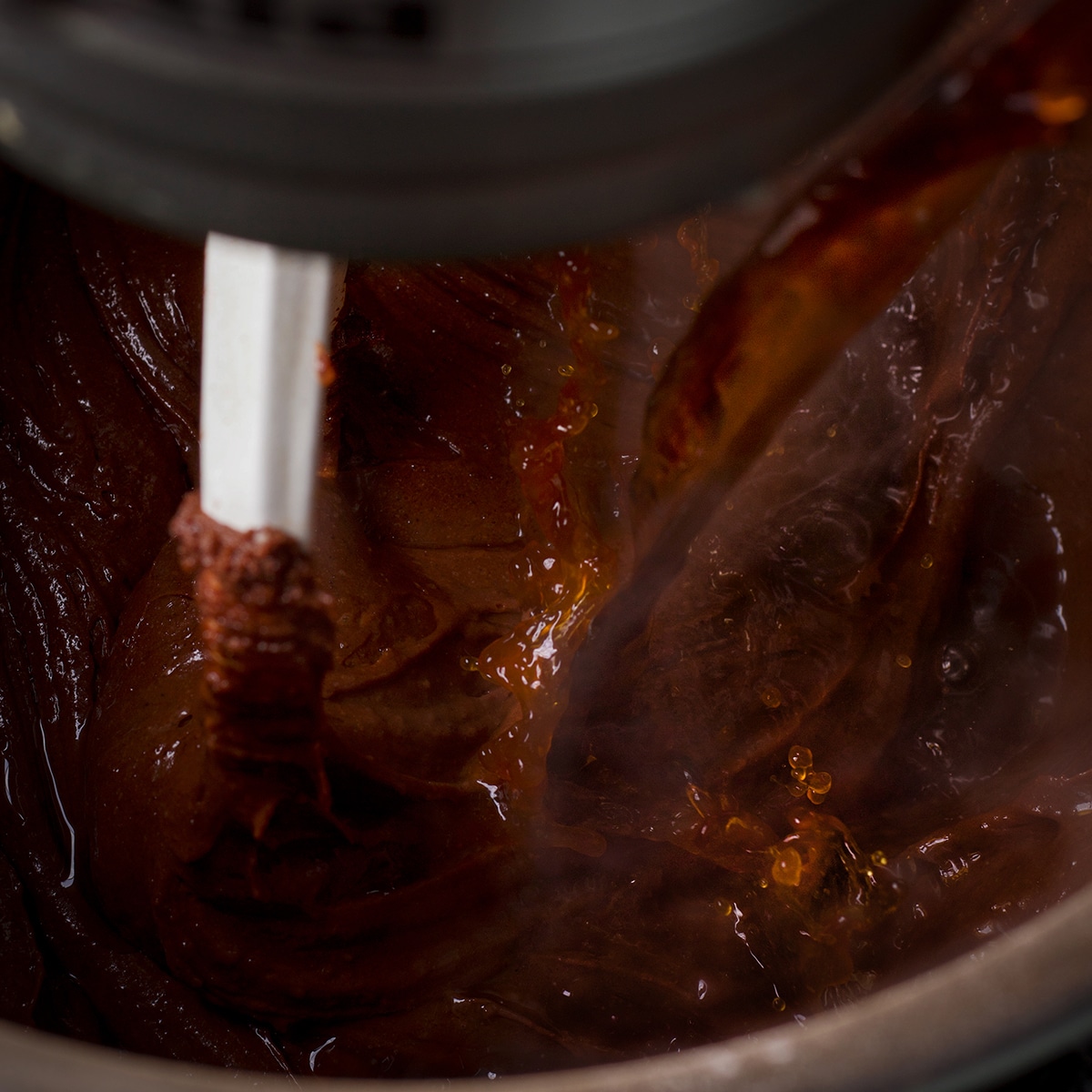 Pouring hot coffee into chocolate cake batter while an electric mixer blends it in.