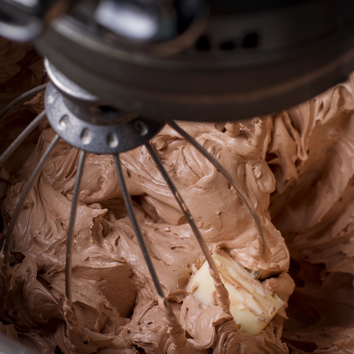 Looking down into a mixing bowl while an electric mixer beats butter into milk chocolate buttercream frosting.