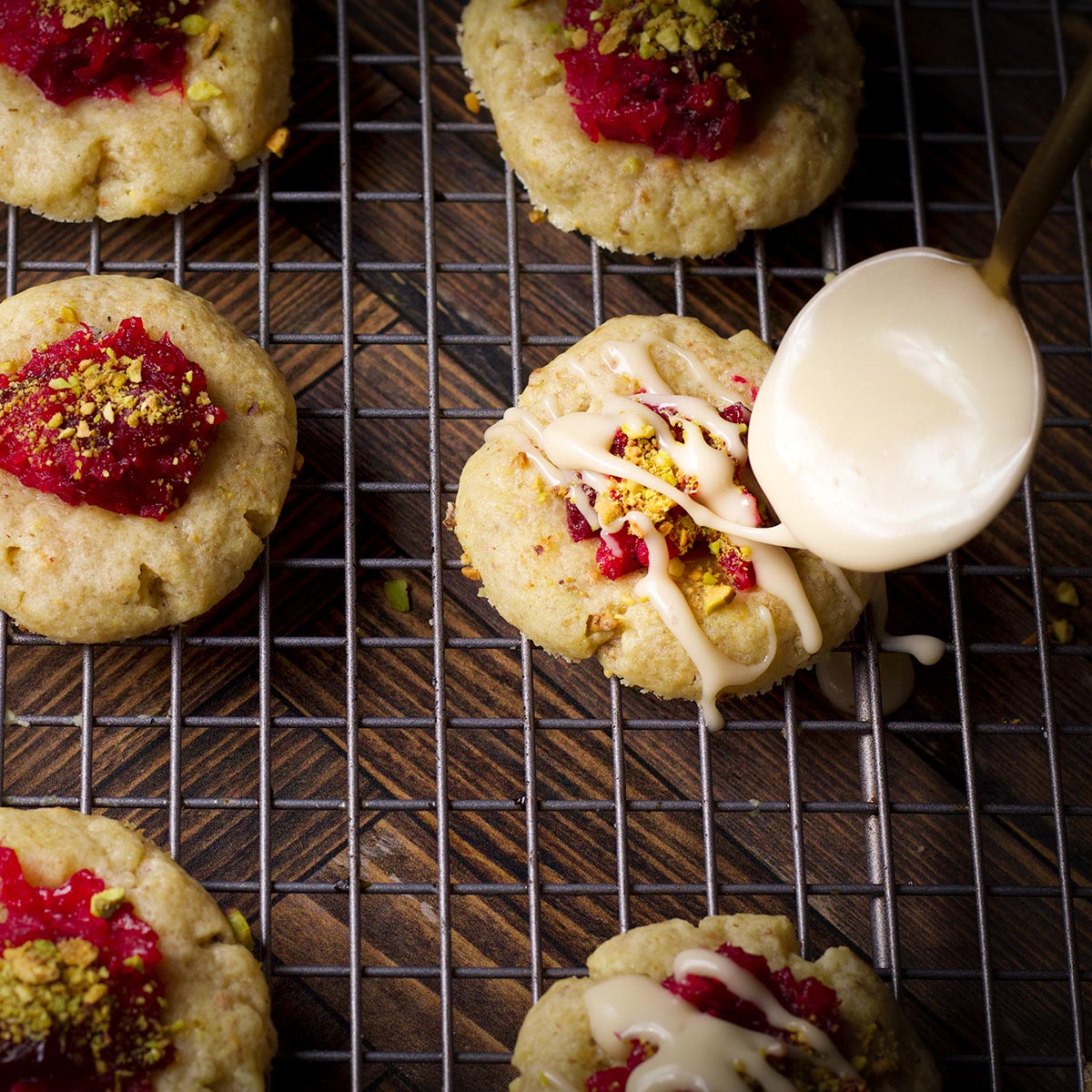 Someone using a small spoon to drizzle vanilla icing over cranberry pistachio cookies.