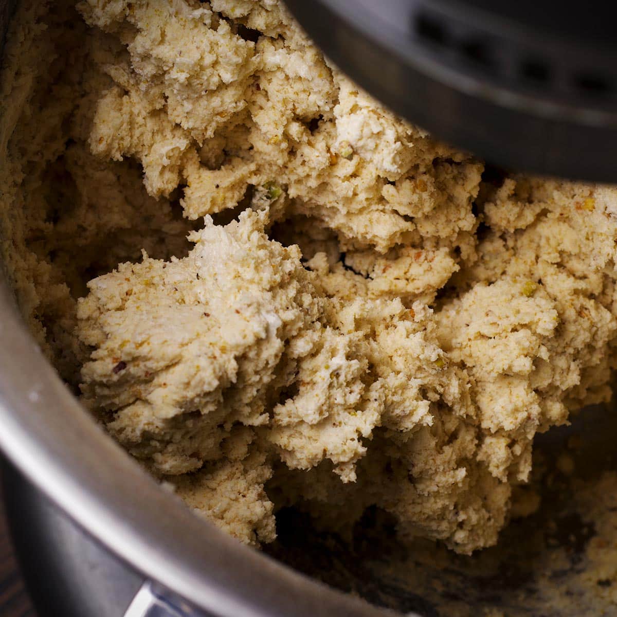 Using an electric mixer to mix flour and ground pistachios into cookie dough.