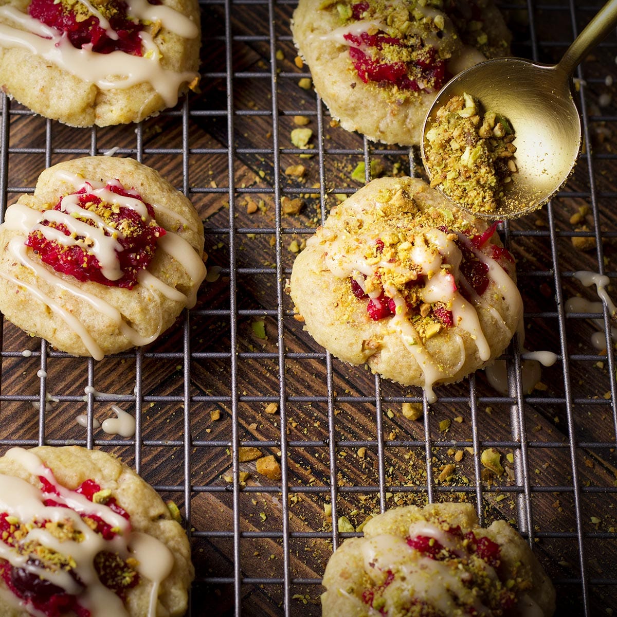 Someone using a gold spoon to sprinkle chopped pistachios over cranberry pistachio cookies.