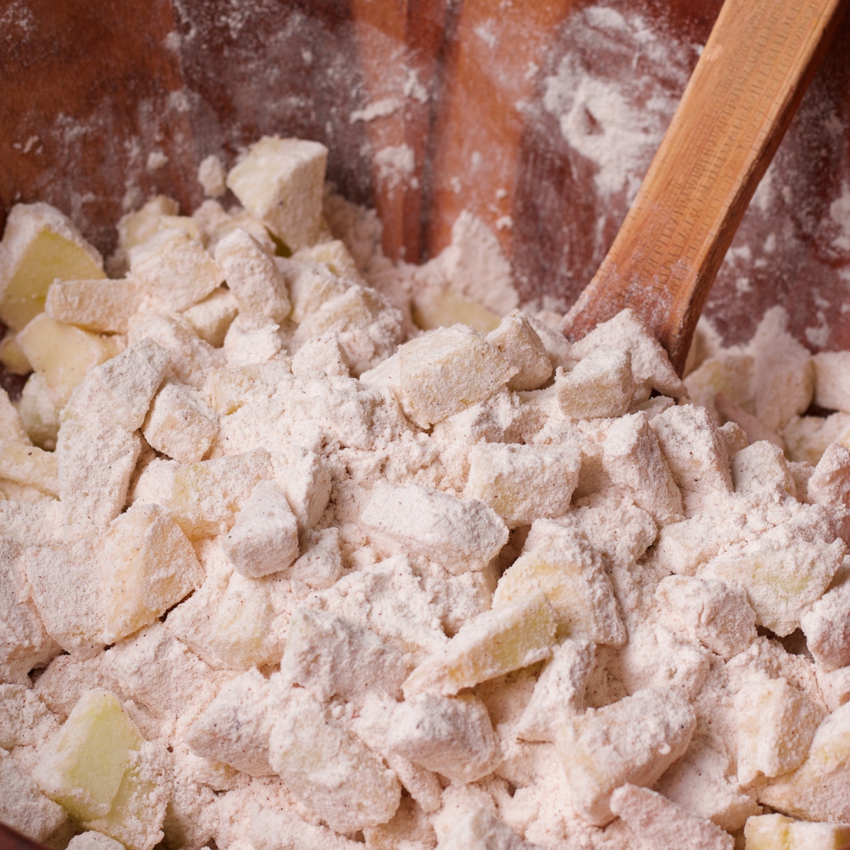 Using a wood spoon to stir chopped apples into flour.