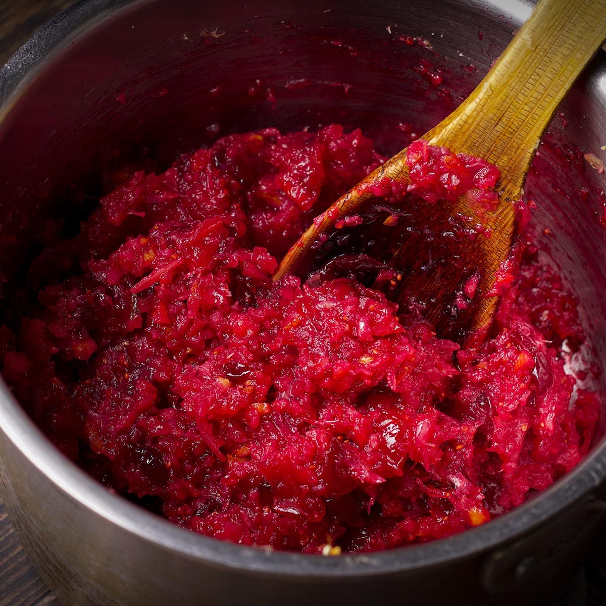 Using a wooden spoon to stir cranberry orange sauce in a saucepan.