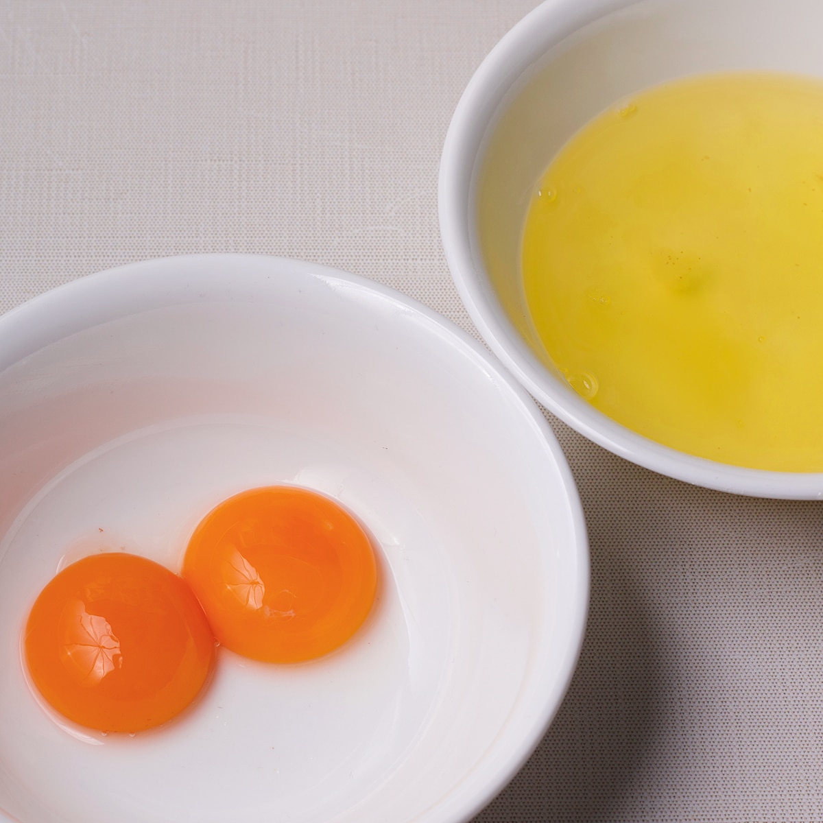 Two white bowls with egg yolks in one and egg whites in another.