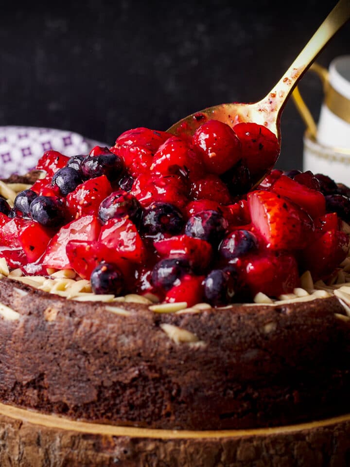 Spooning berry sauce over the top of a chocolate ricotta cake.