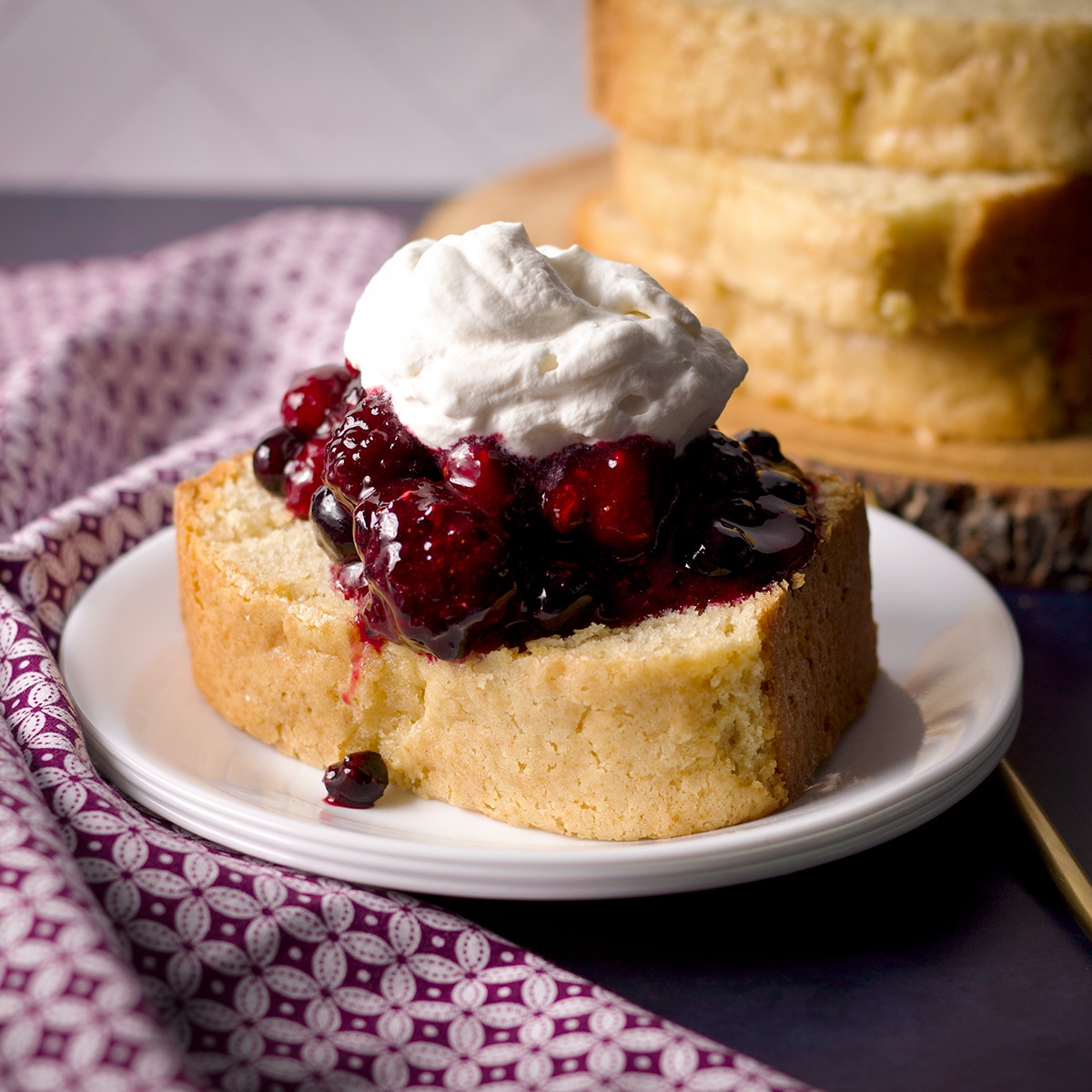 A slice of vanilla loaf cake topped with berry sauce and whipped cream.
