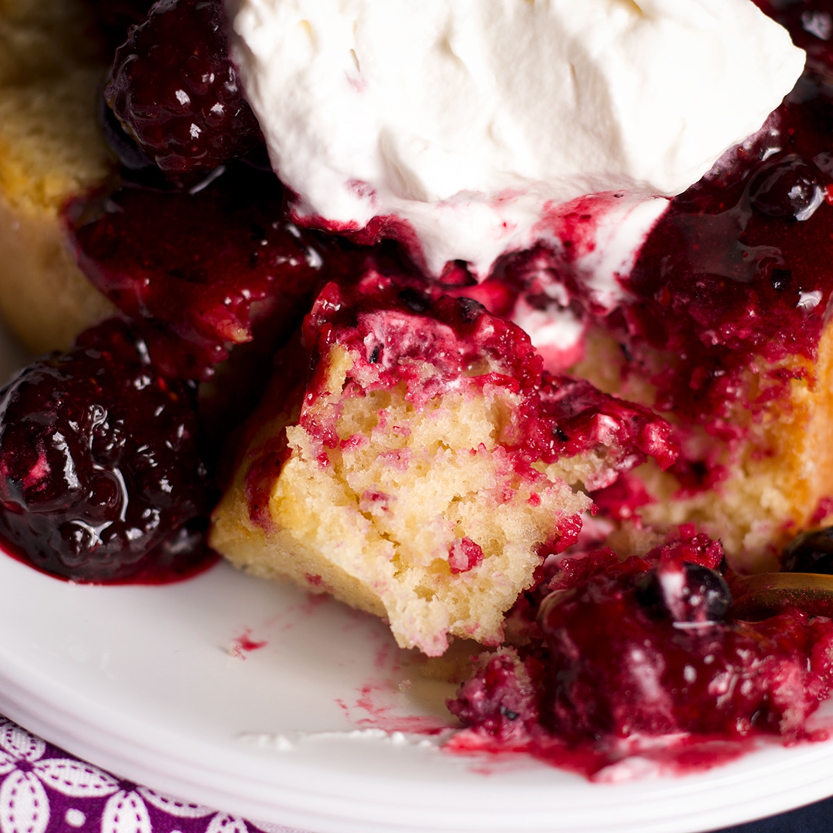 Someone using a fork to cut a bite of vanilla loaf cake covered in berry sauce.