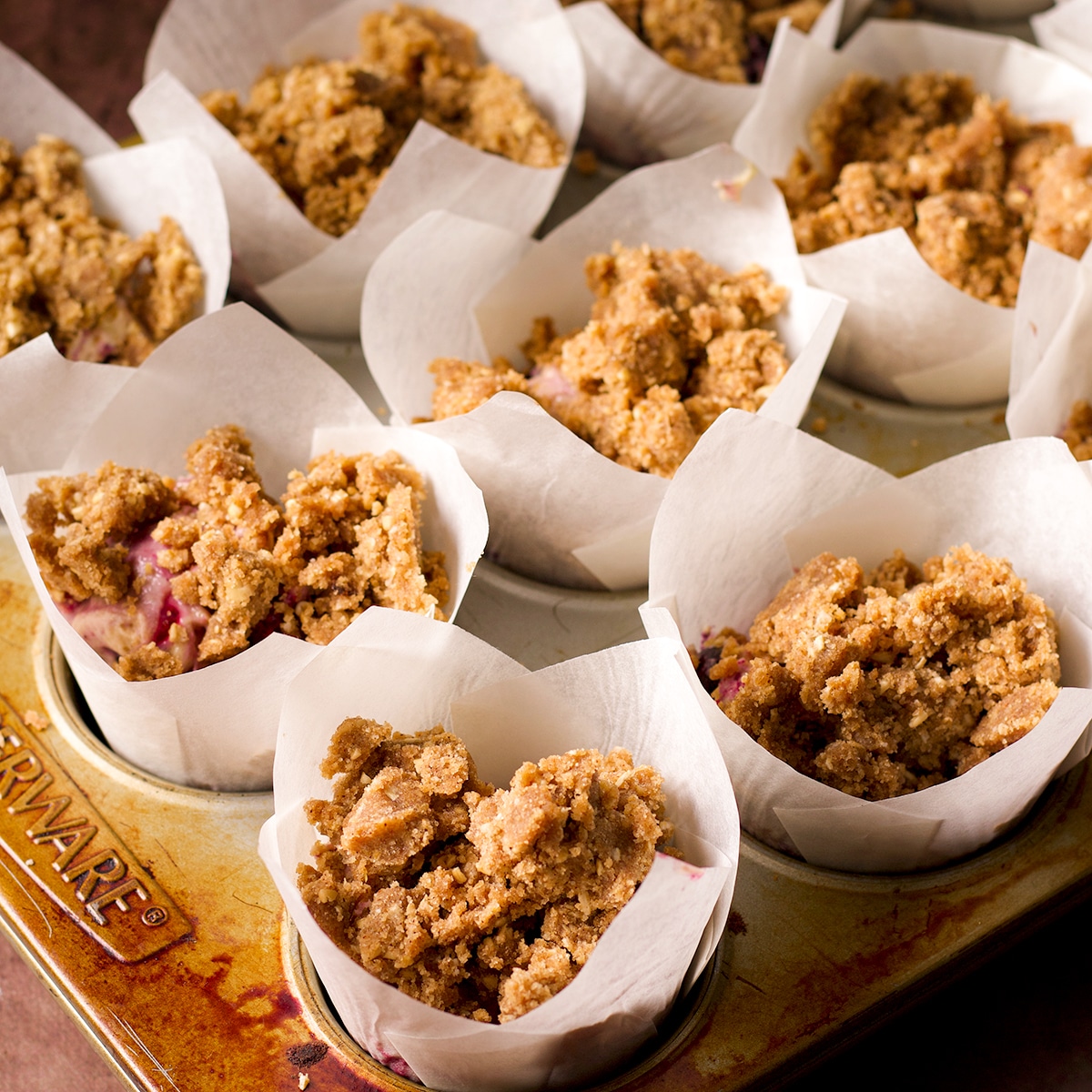 Mixed berry muffin batter distributed evenly between 12 paper-lined muffin cups, topped with streusel, and ready to bake.