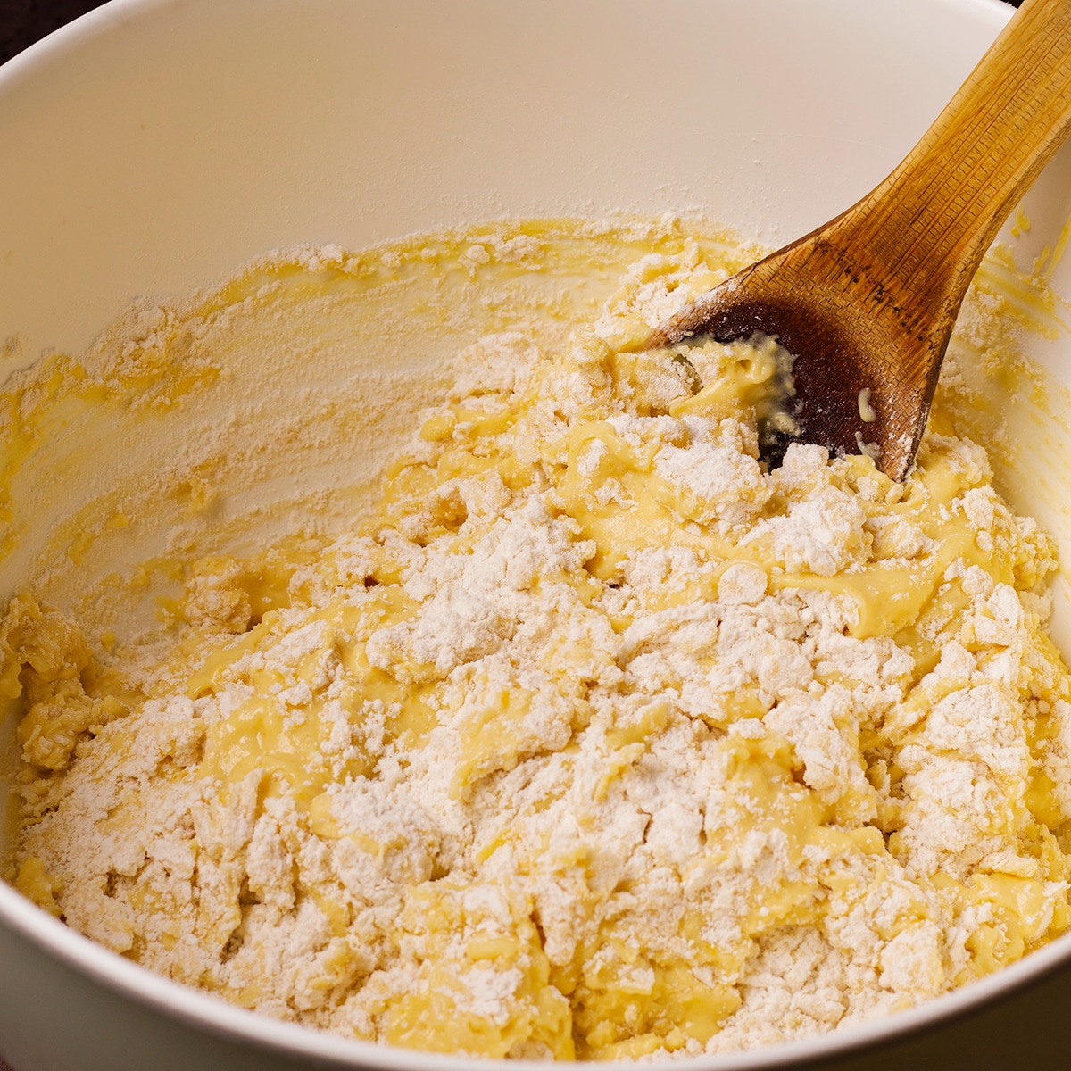 Using a wooden spoon to stir the dry ingredients into the wet ingredients to make muffin batter.