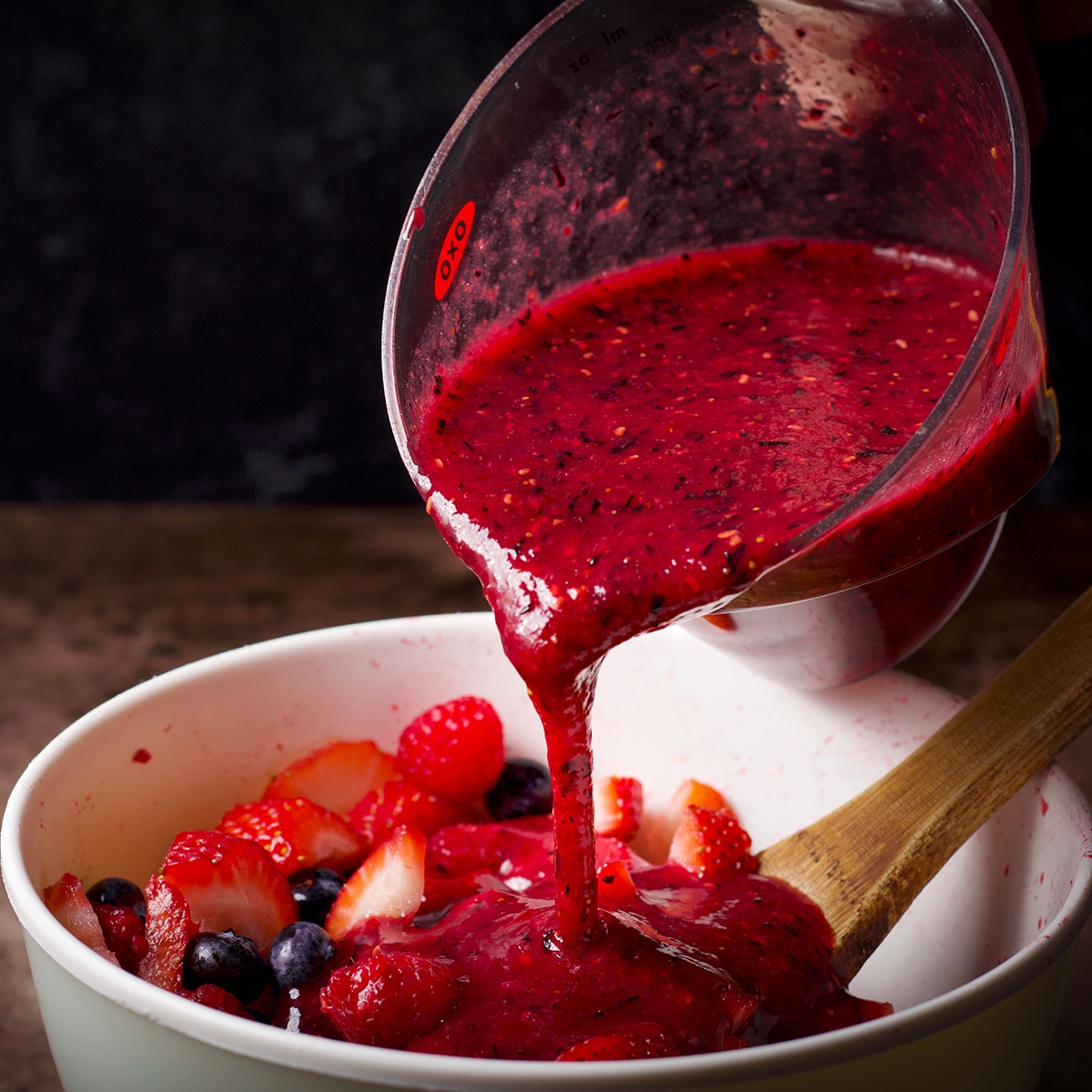 Pouring berry coulis over fresh berries to make a quick berry sauce.