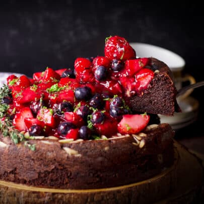 Using a cake server to serve a slice of flourless, gluten-free chocolate ricotta cake covered in fresh berry sauce.