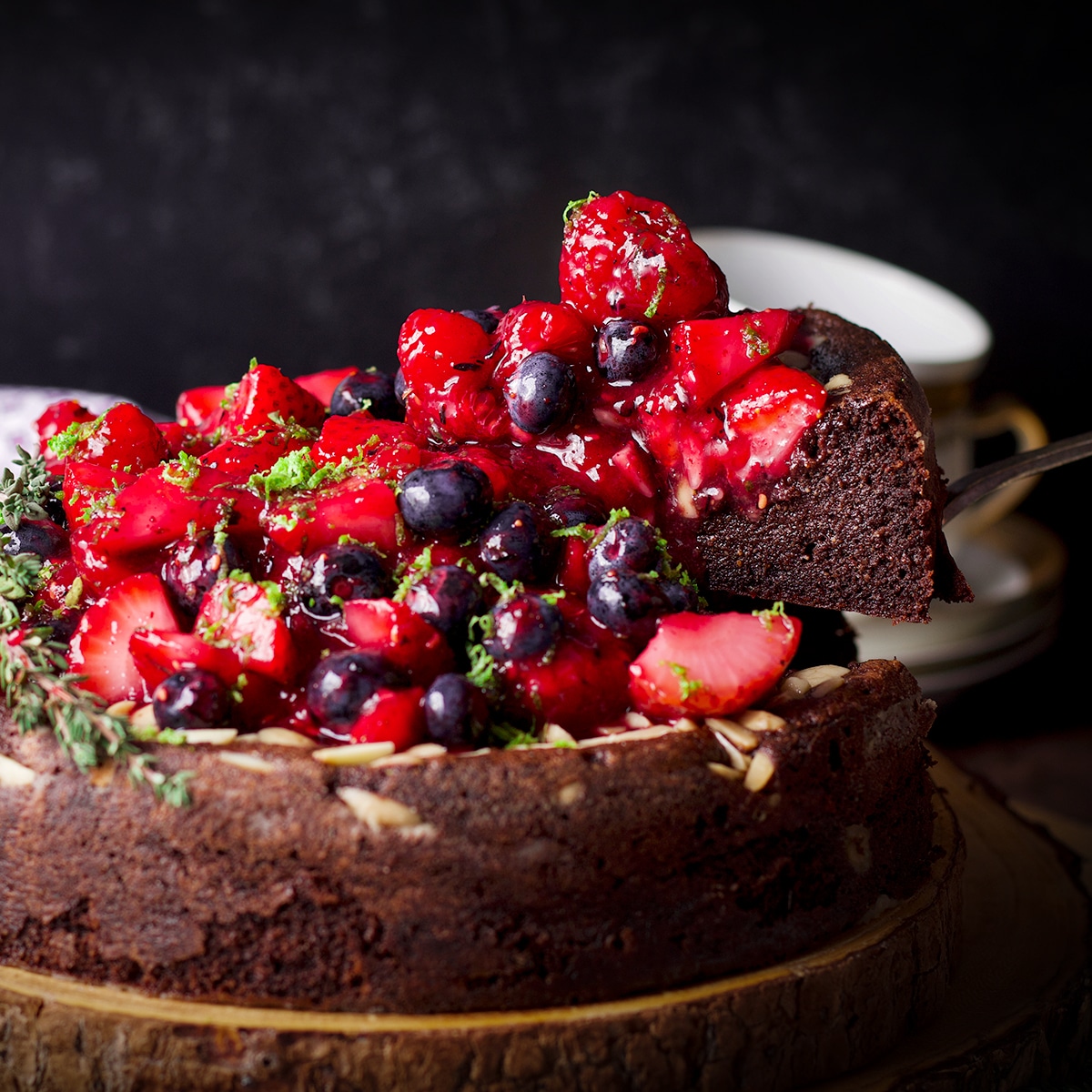 Using a cake server to serve a slice of flourless, gluten-free chocolate ricotta cake covered in fresh berry sauce.