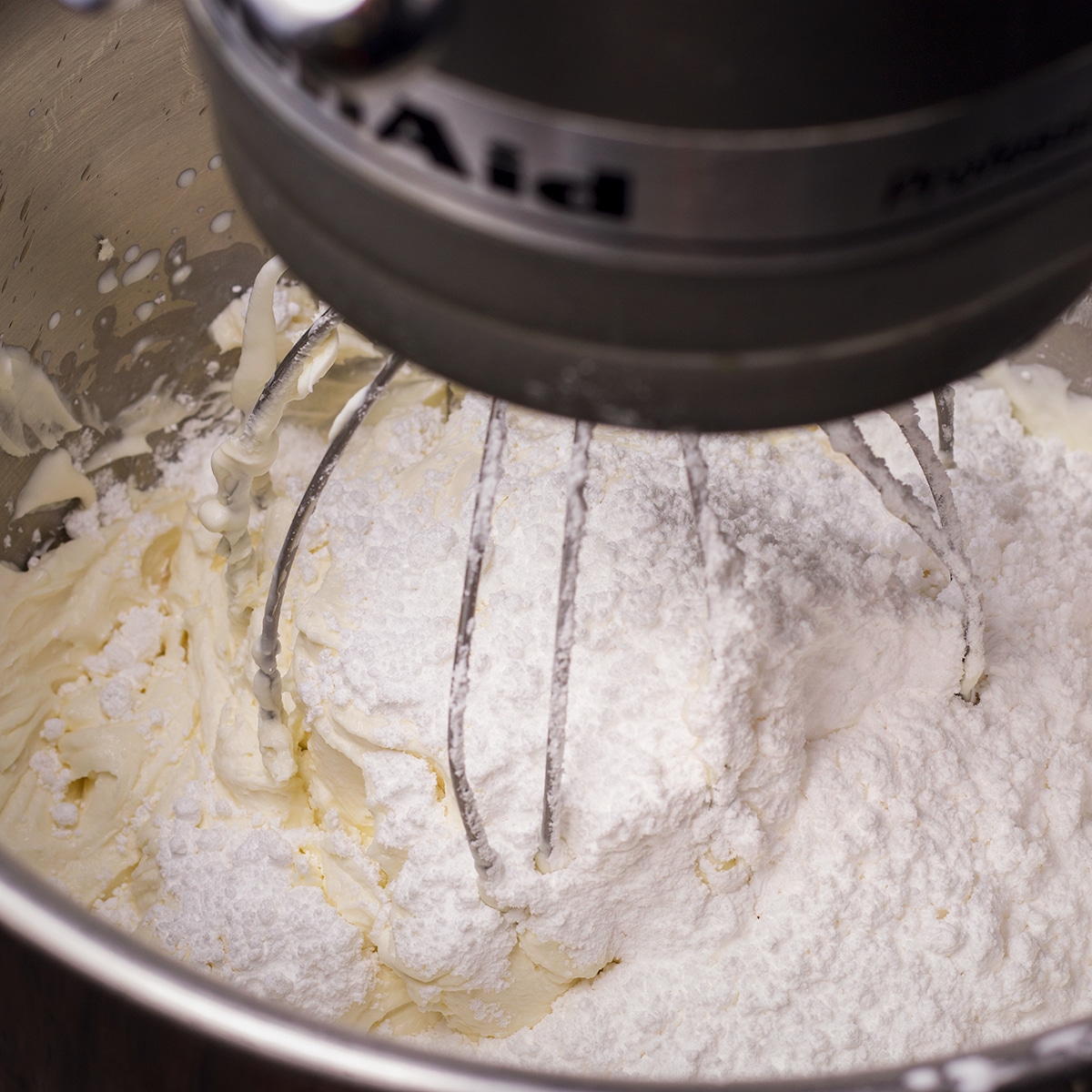 Using an electric mixer to beat powdered sugar into mascarpone frosting.