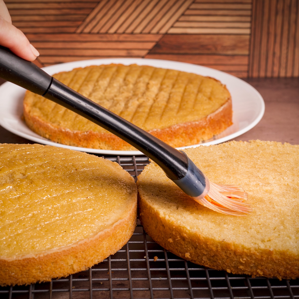 Using a pastry brush to coat orange olive oil cake layers with orange liquor.