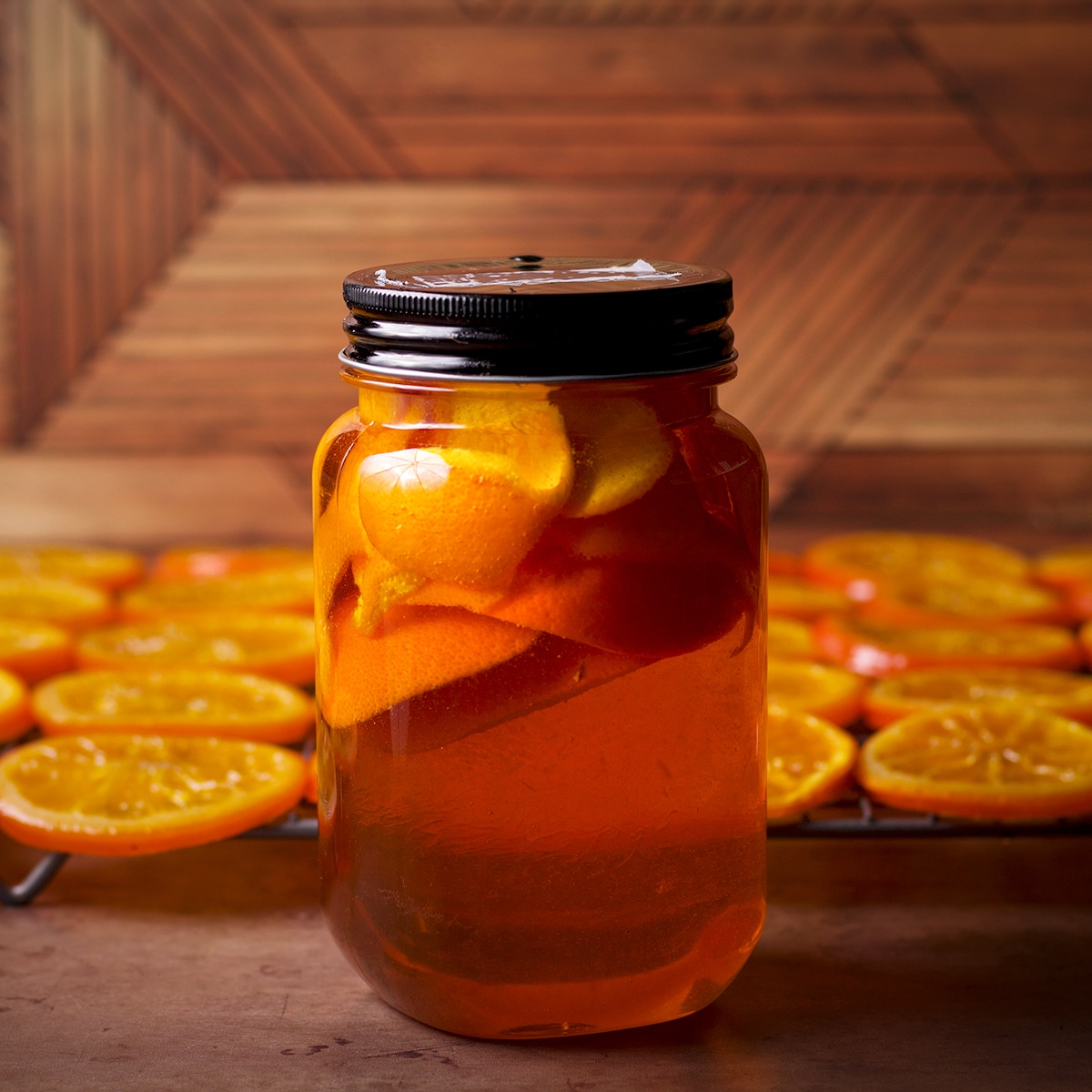 A jar of orange-infused simple syrup in front of a wire rack with candied orange slices drying.