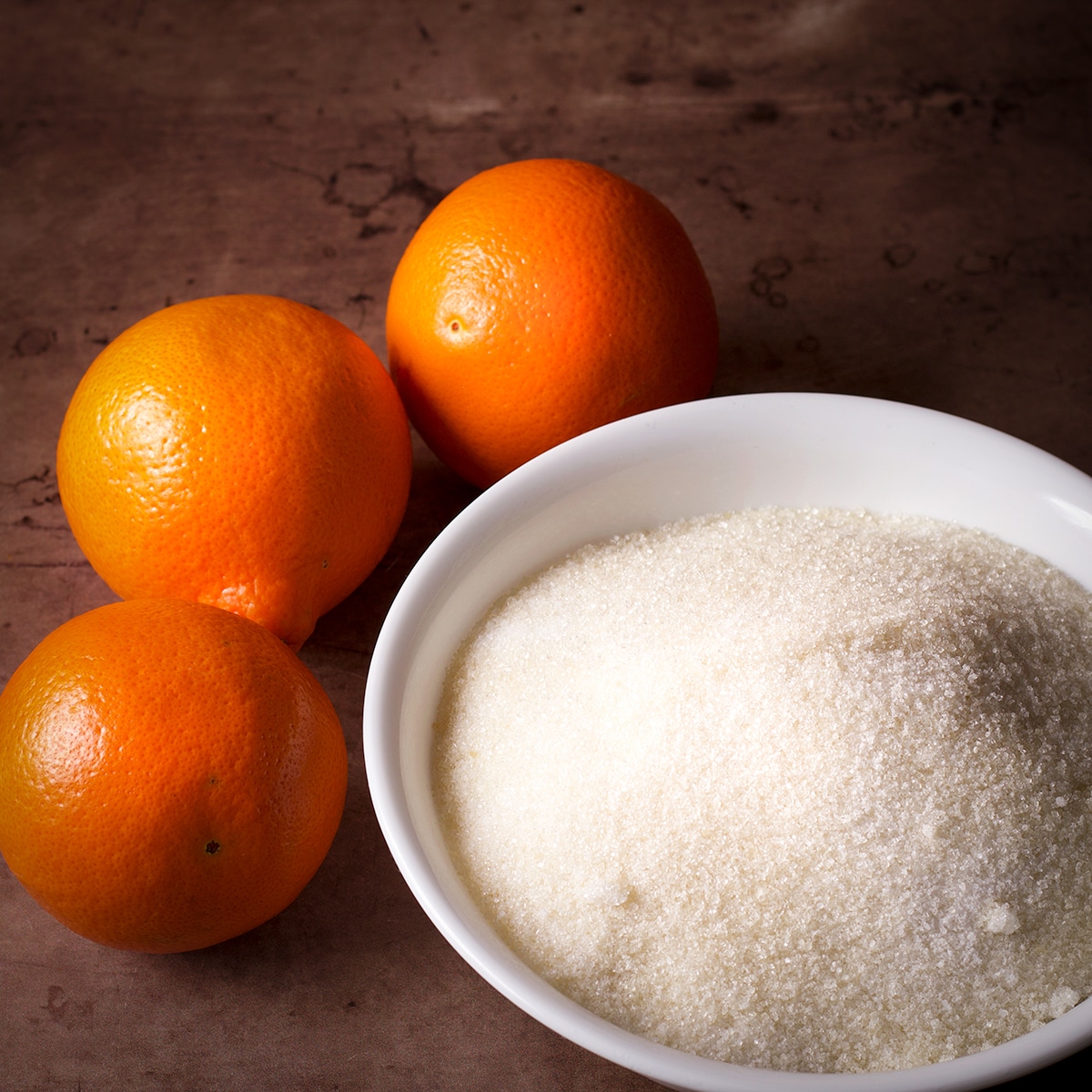 Oranges and a bowl of granulated sugar.
