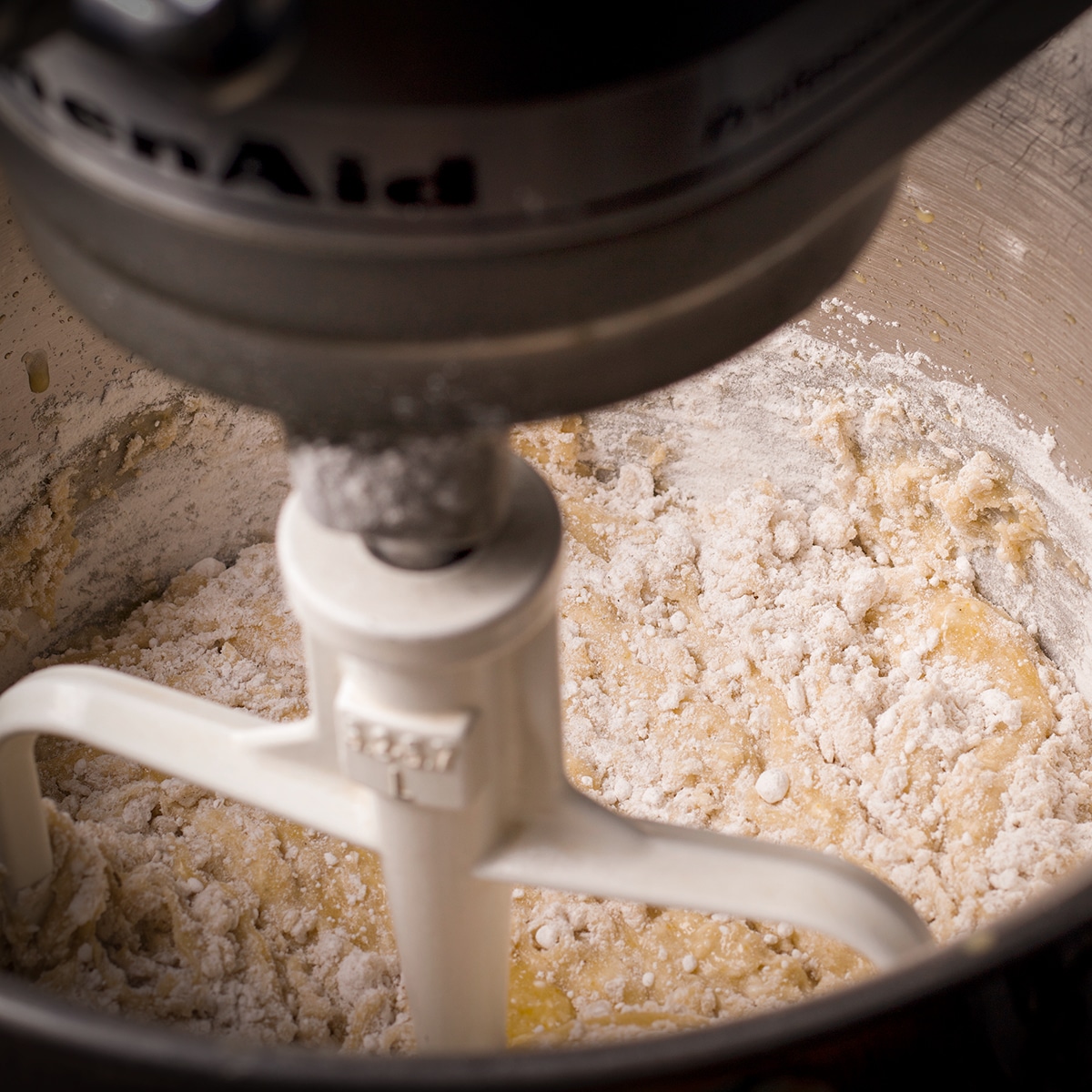 Using an electric mixer to beat flour into orange olive oil cake batter.