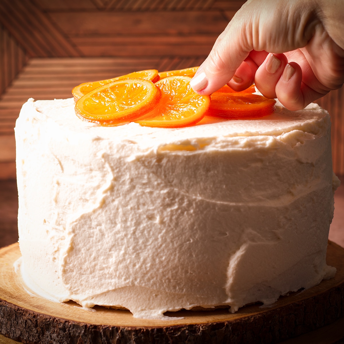 Laying candied orange slices on top of a three-layer orange olive oil cake covered in mascarpone frosting.