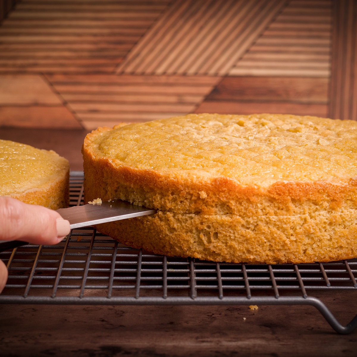 Using a serrated knife to cut a layer of orange olive oil cake in half lengthwise.