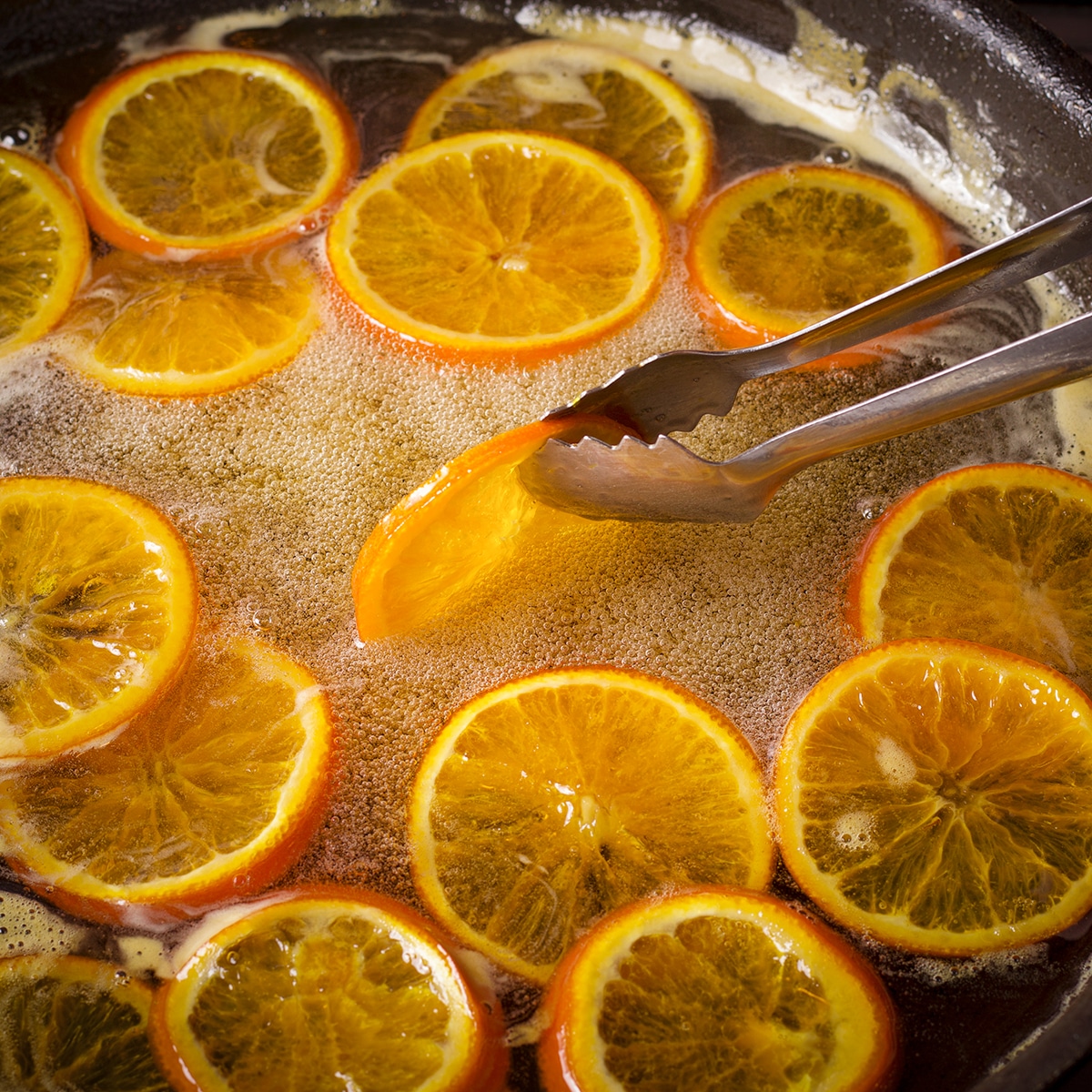 Using metal tongs to turn orange slices in simmering simple syrup.