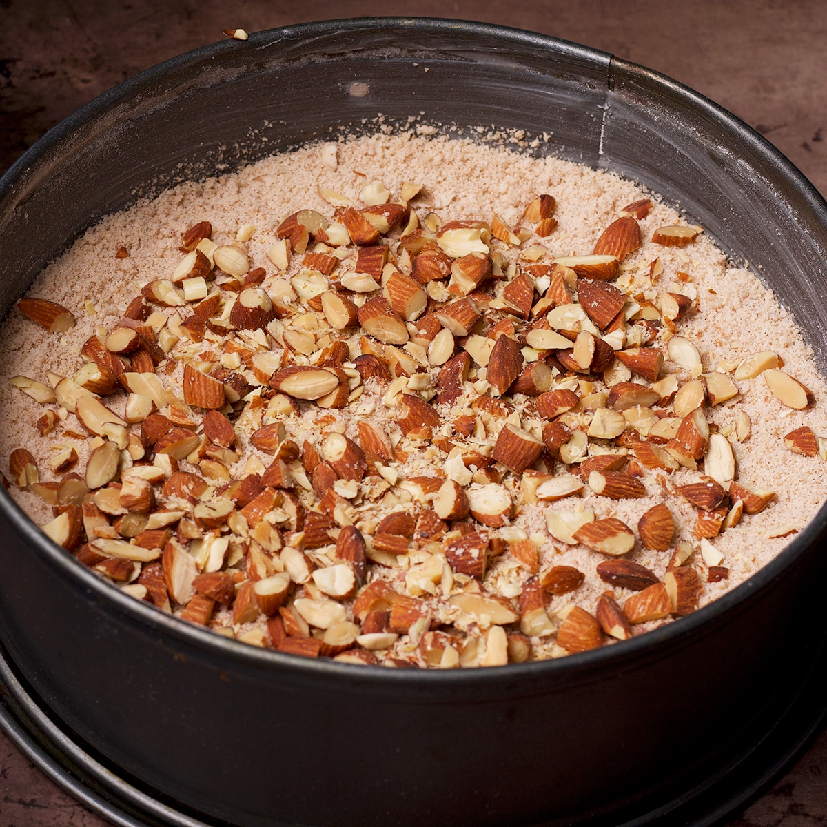 A springform pan containing streusel and chopped almonds.