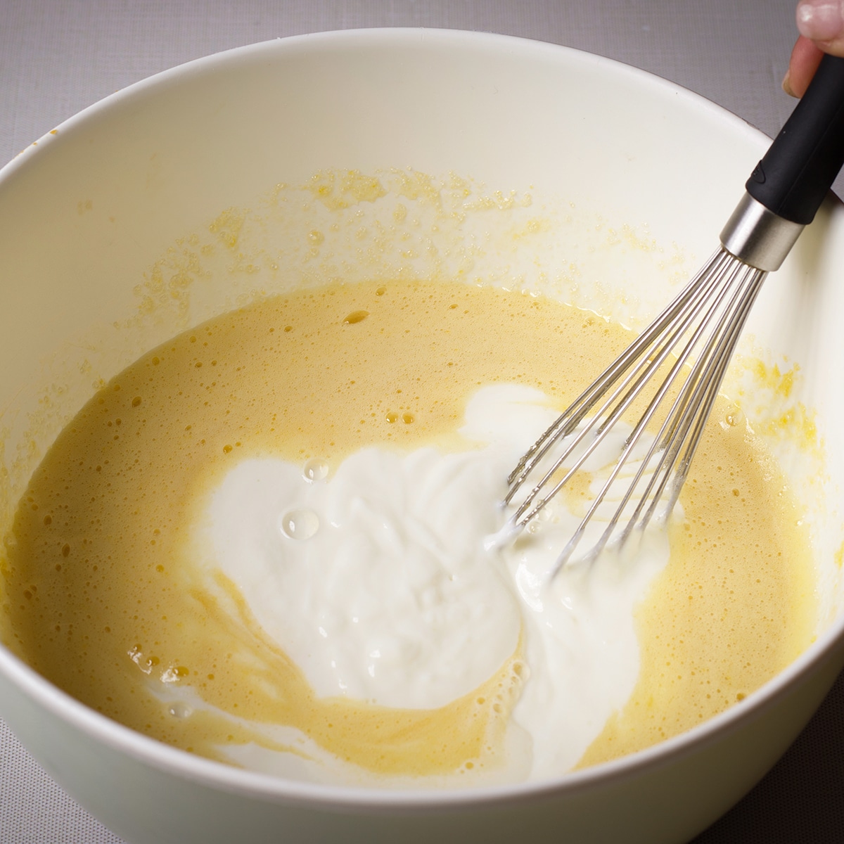 Using a wire whisk to mix yogurt, melted butter, and vanilla into eggs and sugar.