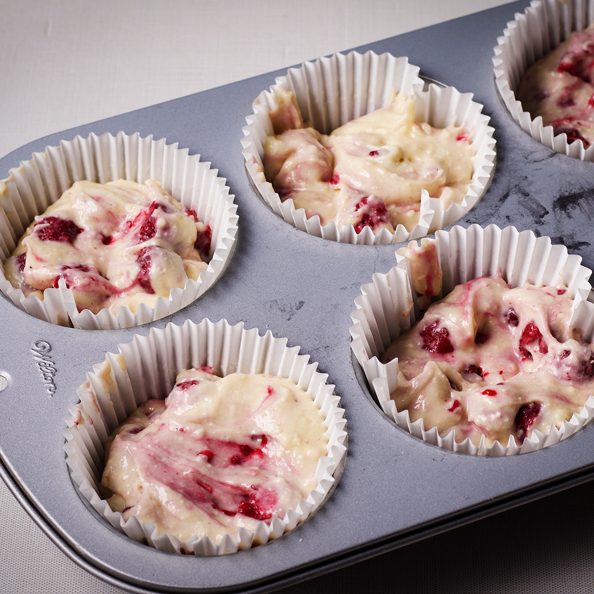 A jumbo size muffin tin fitted with paper liners that are filled with raspberry muffin batter.