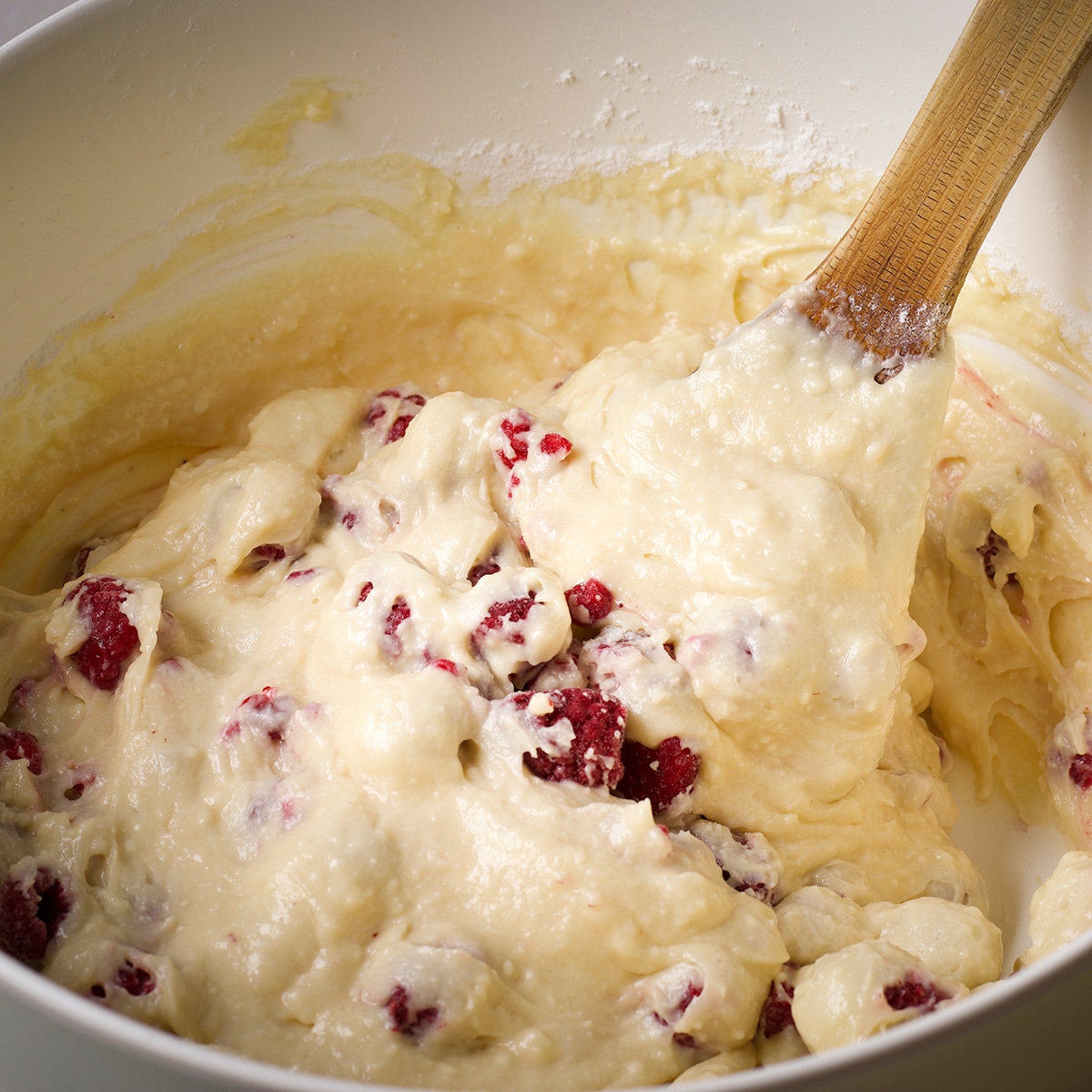 Using a wooden spoon to fold raspberries into muffin batter.