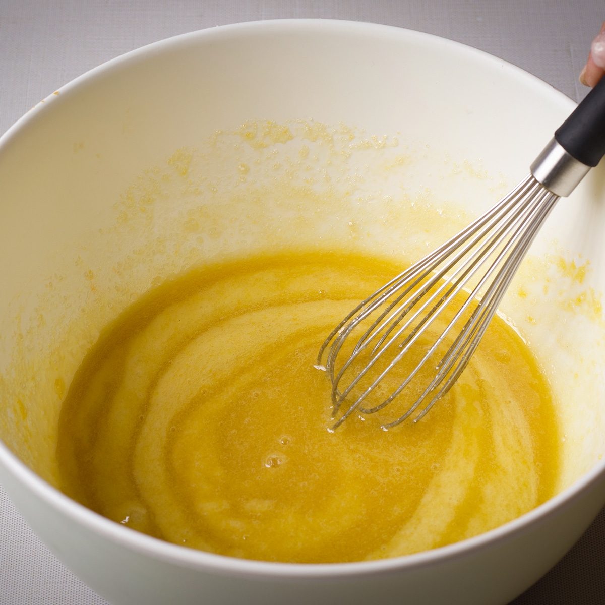 Using a wire whisk to beat eggs and sugar in a bowl.