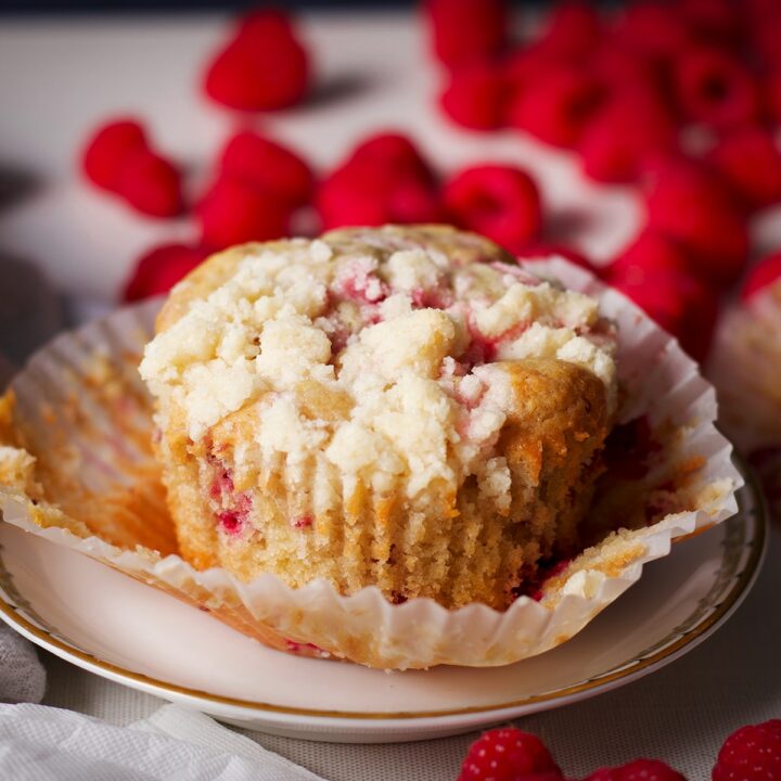 A large raspberry muffin on a plate surrounded by fresh raspberries.
