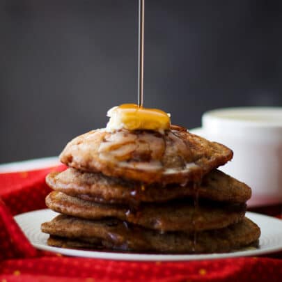 Pouring maple syrup over a stack of apple cinnamon pancakes.