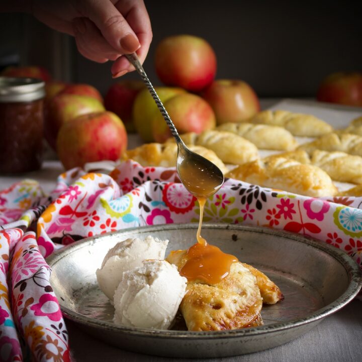 Using a spoon to drizzle salted caramel sauce over two apple butter hand pies on a tin plate.