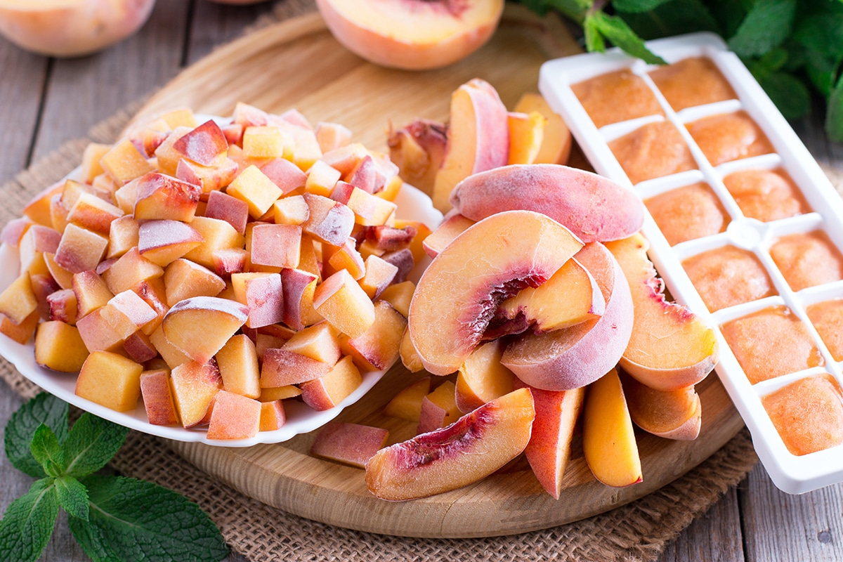 A bowl of frozen peach chunks next to sliced frozen peaches and an ice cube tray filled with frozen peach puree.
