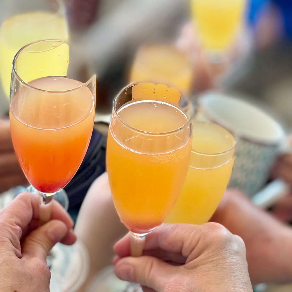 Several people holding champagne glasses filled with peach puree and champagne.